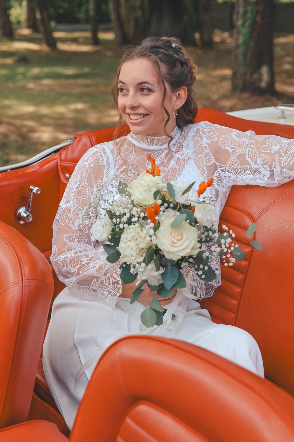 La mariée souriante, son bouquet à la main, dans une voiture orange